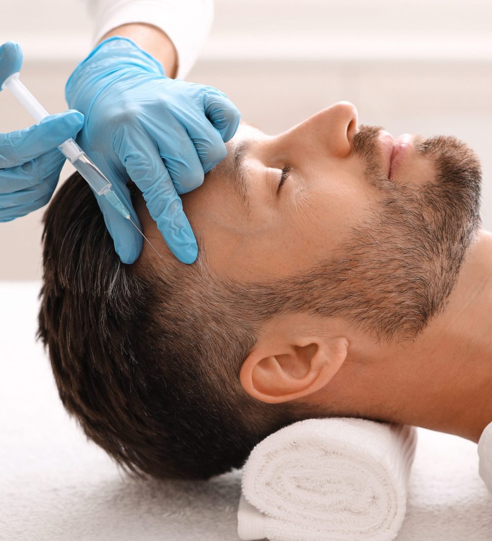 Side view of handsome middle aged man getting hair treatment at beauty salon. Man having mesotherapy session at aesthetic clinic, therapist hands in gloves making injection in scalp, closeup